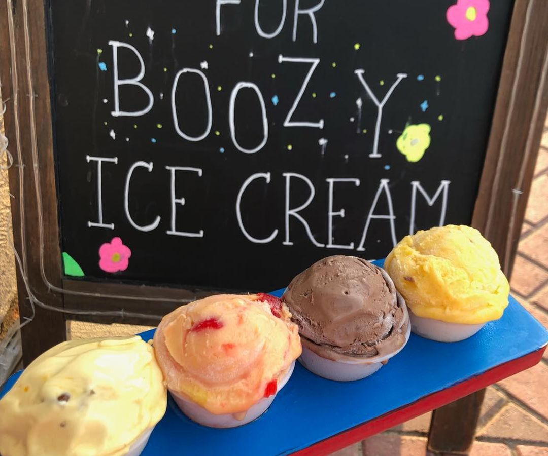 Four cartons of boozy ice cream in front of a chalk board that reads, “The time has come for boozy ice cream.” 