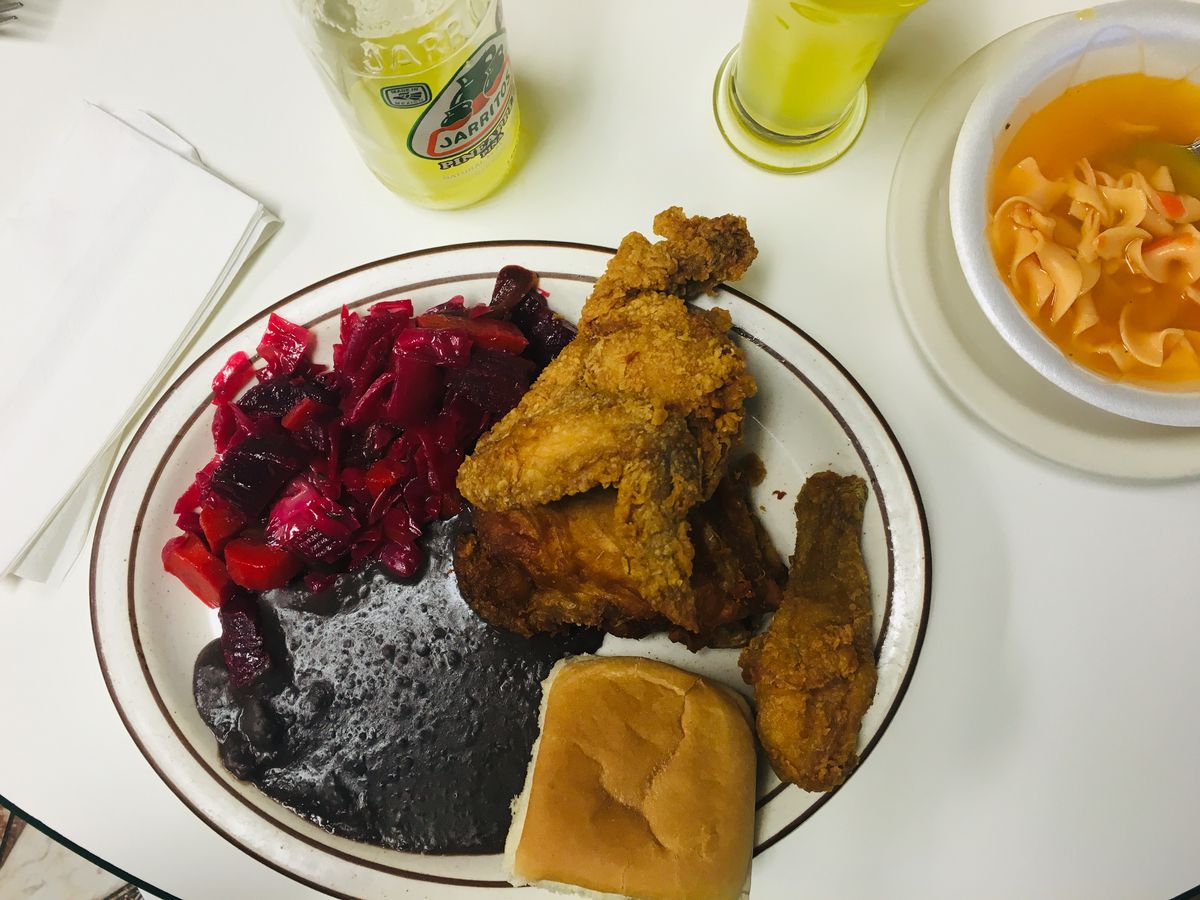 Fried chicken on a plate with black beans, a roll, and purple cabbage slaw.