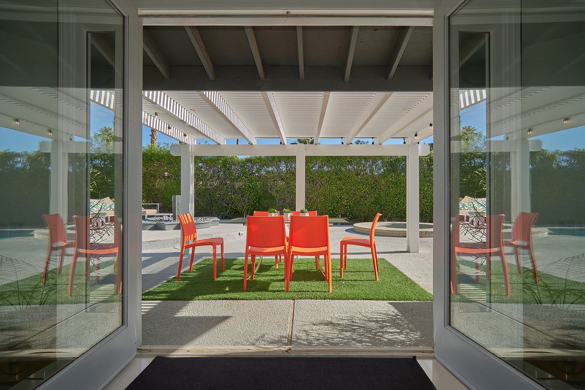Glass white doors open up onto a covered pergola with an orange dining set underneath. 