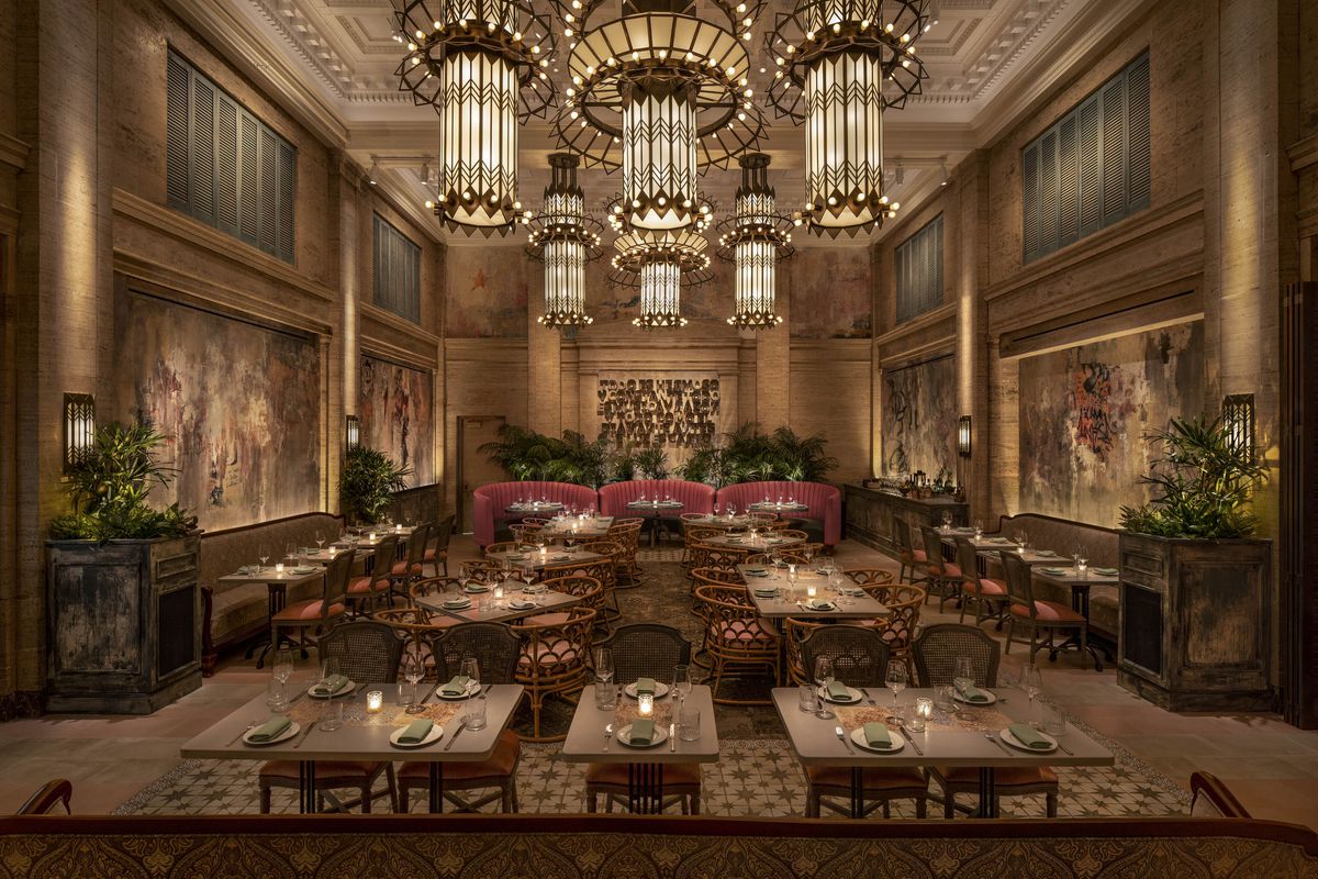 A high-ceilinged restaurant with grand chandeliers, red plush seating, and wood accents