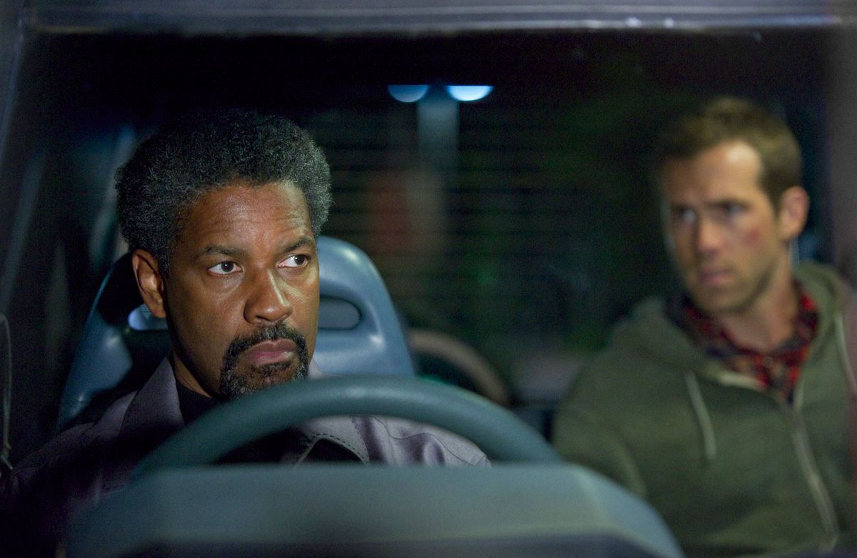 Tobin Frost (Denzel Washington) sits in the front seat of a van with Matt Weston (Ryan Reynolds) in the background.