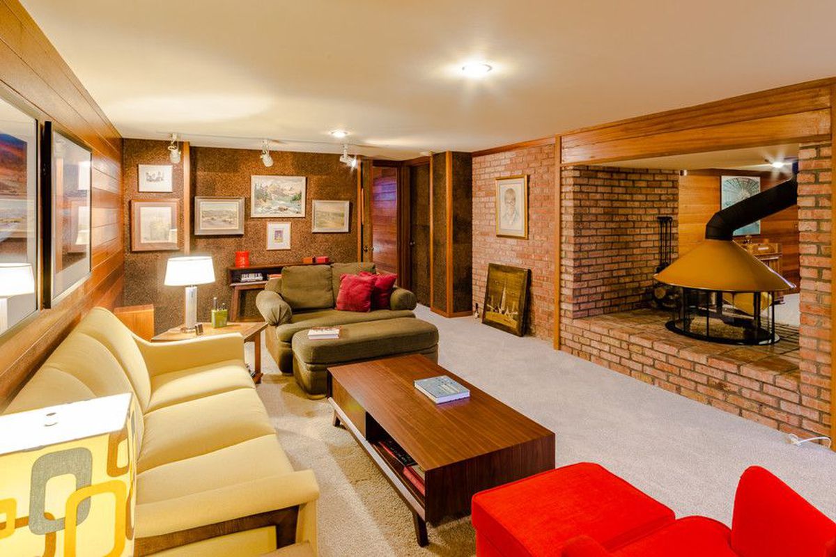 Interior shot of lounge with wood paneled walls and exposed brick and a round fireplace set into a cubby. 