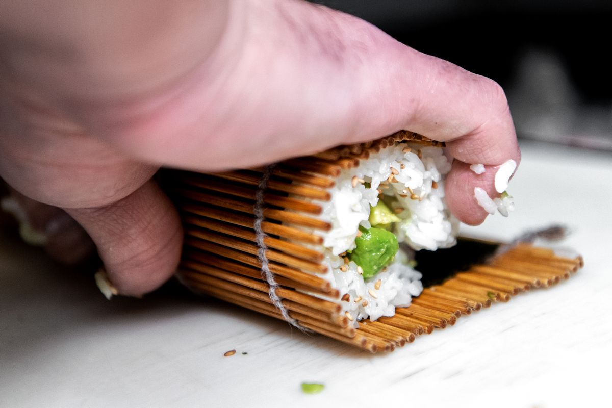 A chef makes a sushi hand roll using a wooden tool.