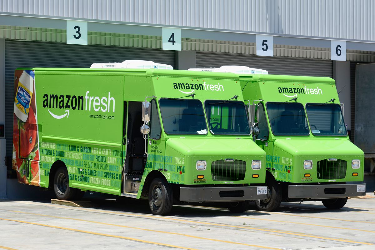 Amazon Fresh delivery trucks sit parked at a warehouse