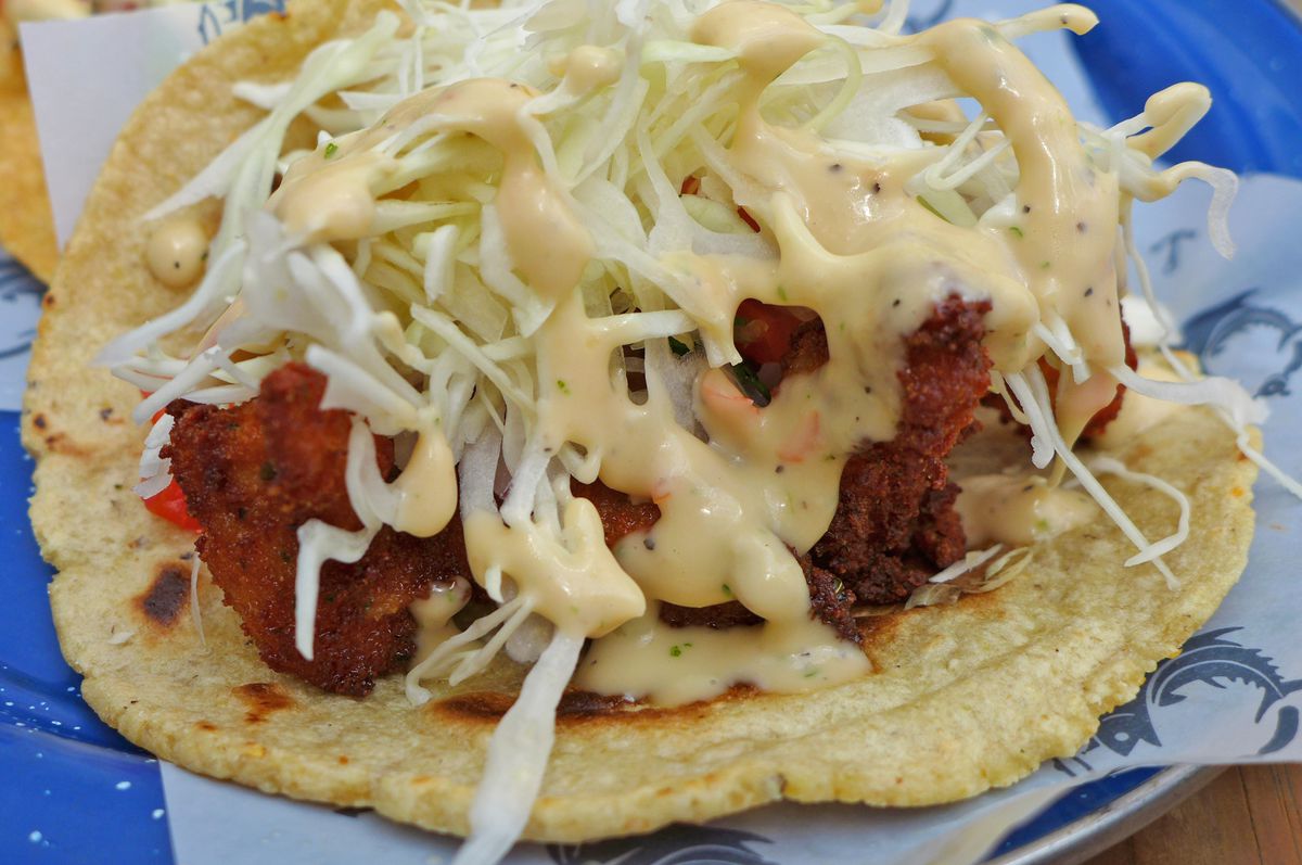 A taco splayed open to show dark red shrimp and cabbage.