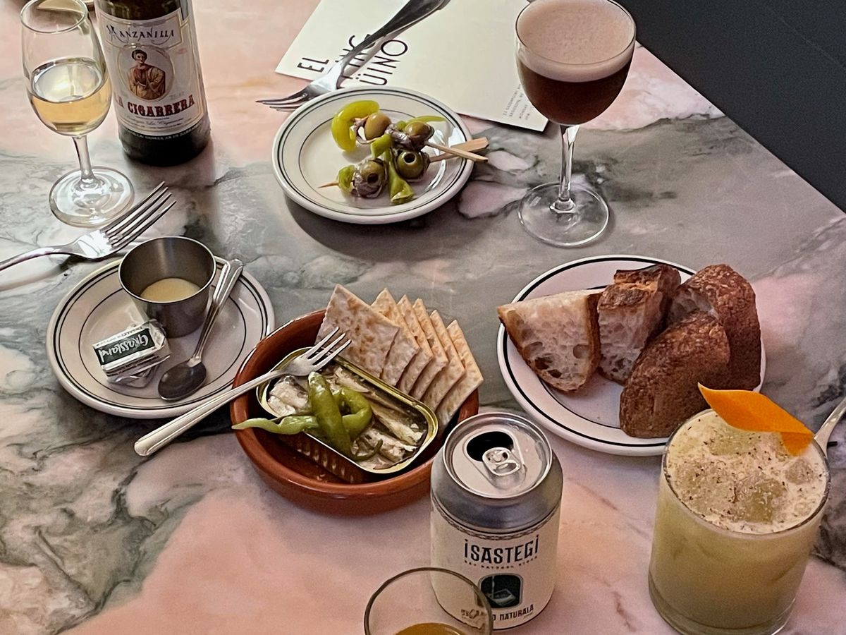 Saltines, tinned fish, and skewers of pickled vegetables are arranged on a table beside glasses of wine at El Pingüino, a restaurant in Greenpoint.