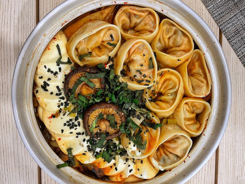 Round dumplings in a hot pot with rice cakes, mushrooms, herbs, and broth.