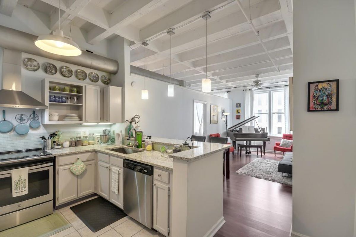 A big white loft area with a kitchen at left and a piano at right.