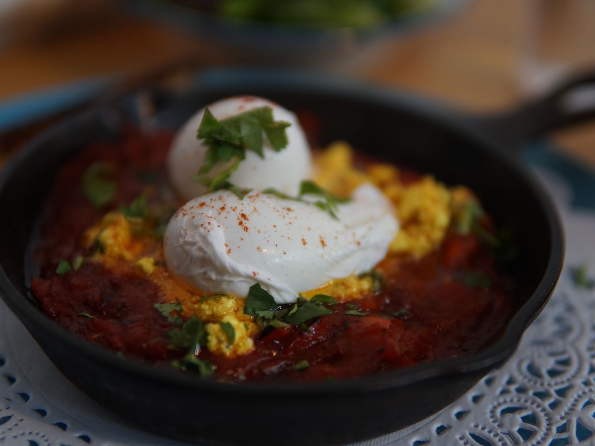 A cast-iron with a handle has yellow yolk and two poached eggs sitting over a stew of red sauce.