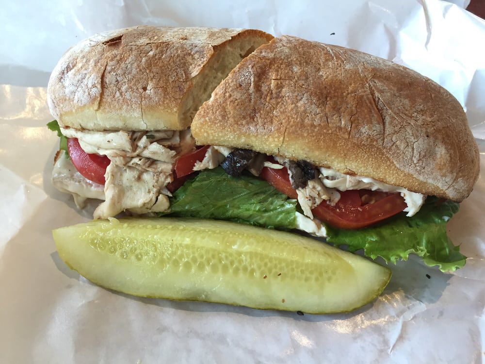 A hoagie stuffed with slice turkey, lettuce, and tomato with a dill pickle laying in front of it. 