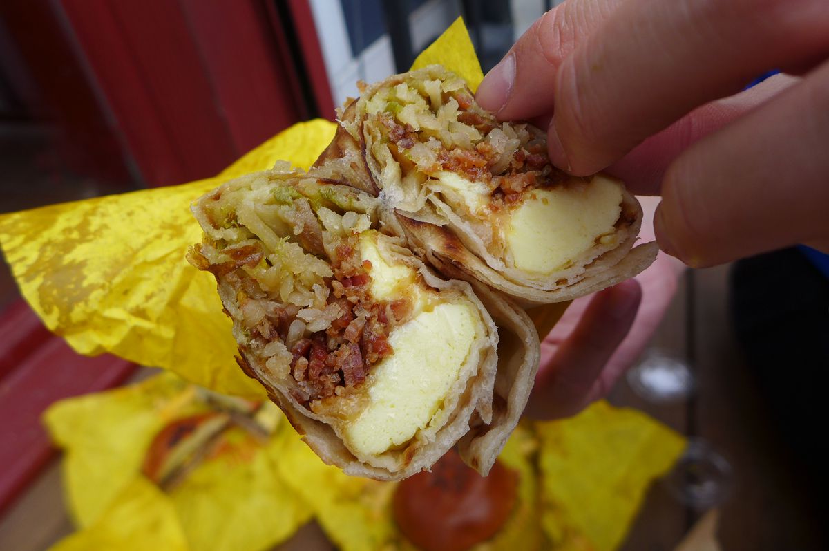 A burrito cut in half with a blue sleeved hand poking it.