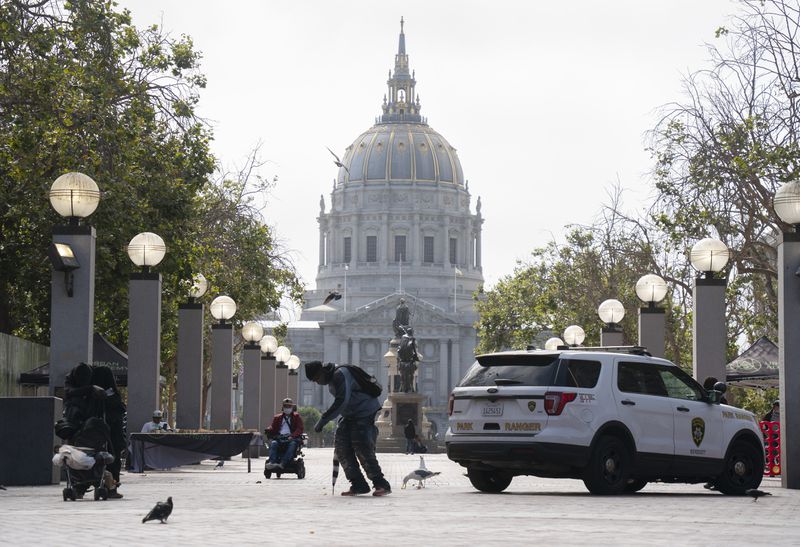 San Francisco City Hall with an unhoused man walking in the foreground.
