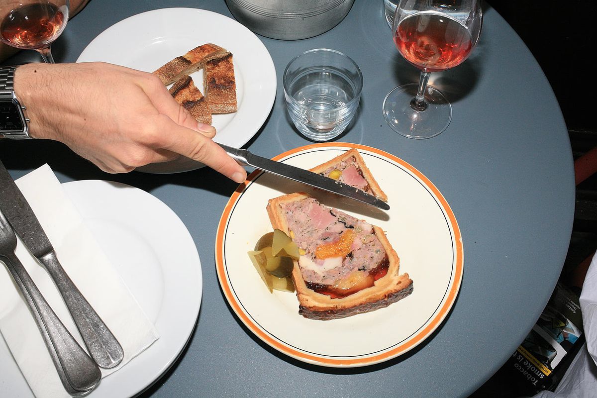 A hand cuts into a slice of paté en croute with a knife.