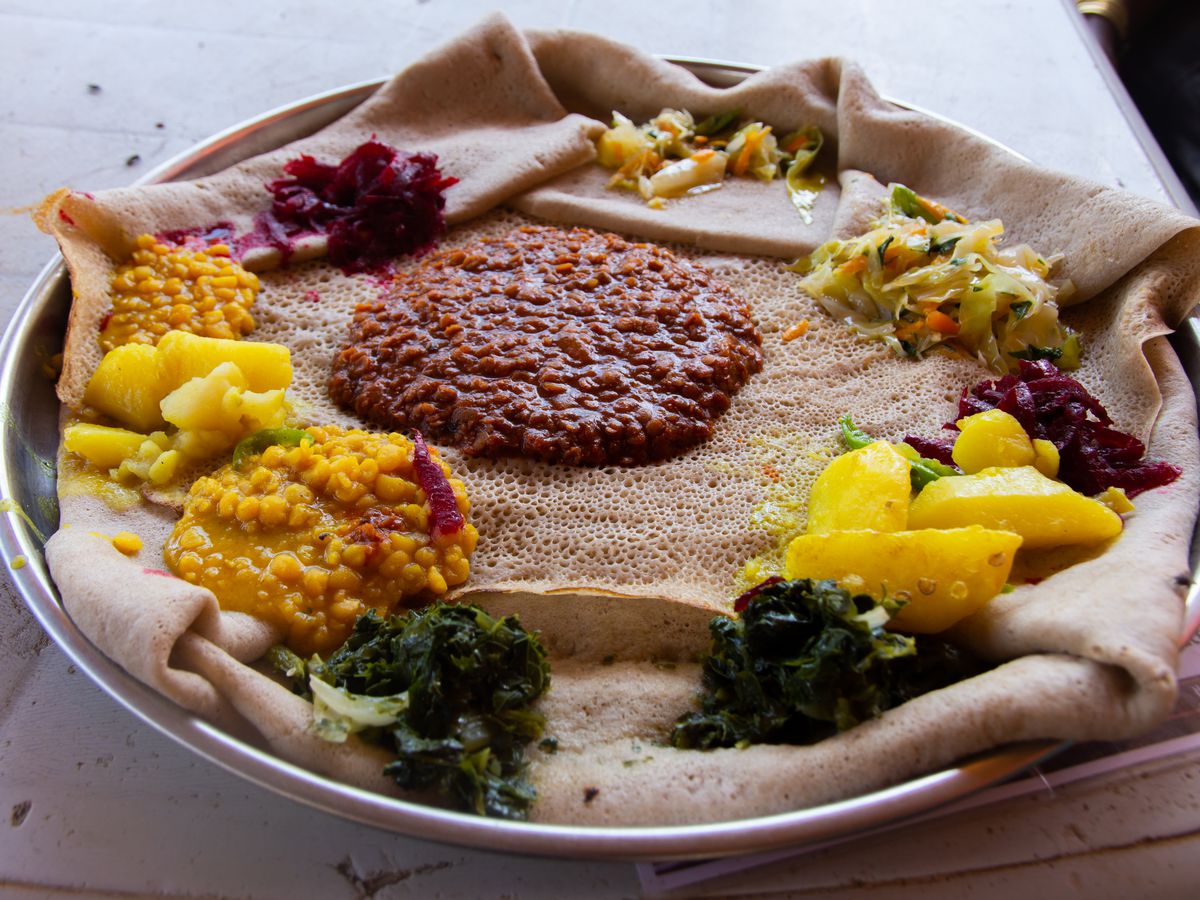 A platter is lined with Ethiopian injera bread and topped with various colorful sauces and stews