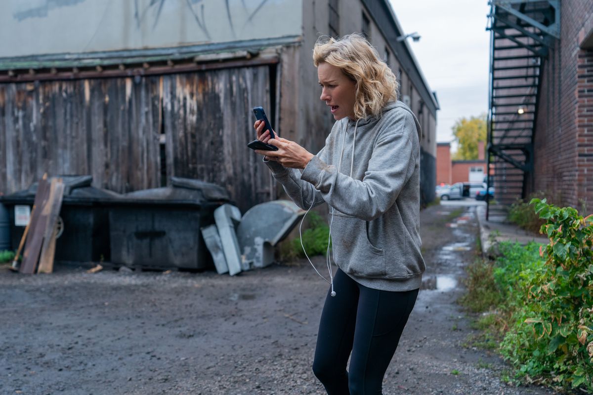 Naomi Watts shouts anxiously at her phone in a back alley