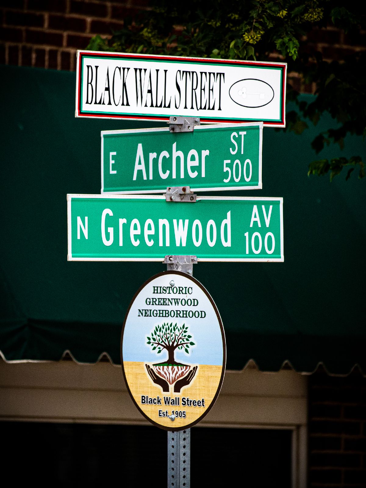 A pole with street signs — Black Wall Street, Archer Street, Greenwood Street — and a plaque that says “Historic Greenwood Neighborhood.”