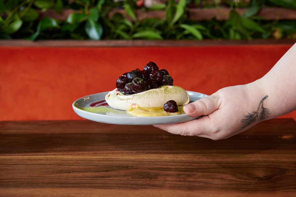 A hand drops a plate of pavlova topped with cherries at a table at Jojo.
