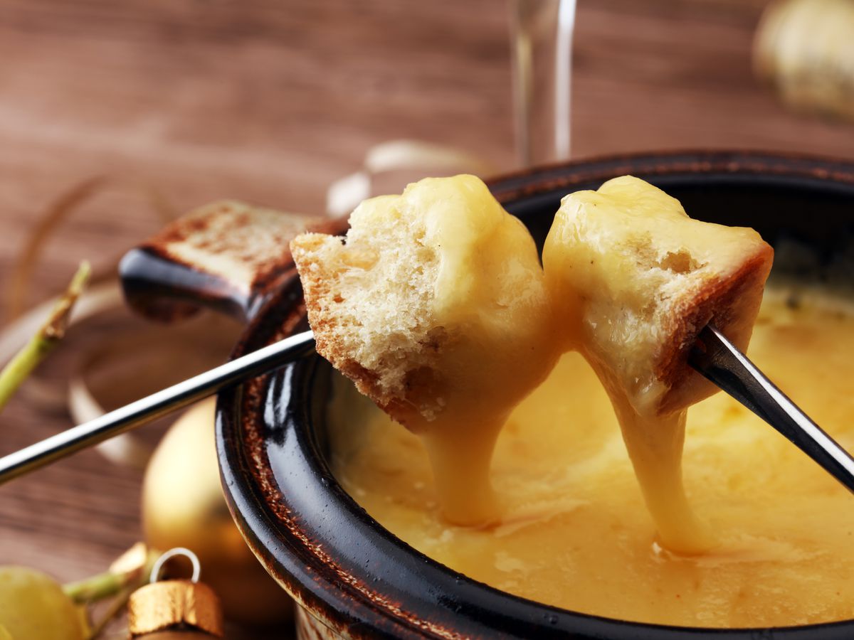 Two forks dunk bread in a fondue pot.