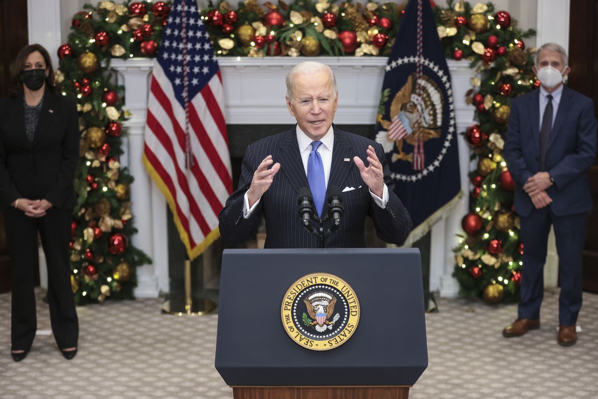 President Joe Biden speaks from a lectern in front of a White House fireplace decorated for Christmas.