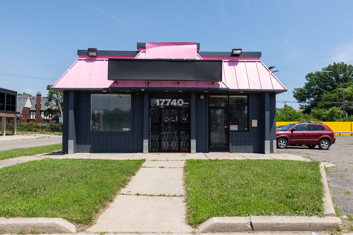 The view of Pink Flamingo from Woodward Avenue features grass and an black building with a bright pink roof. 