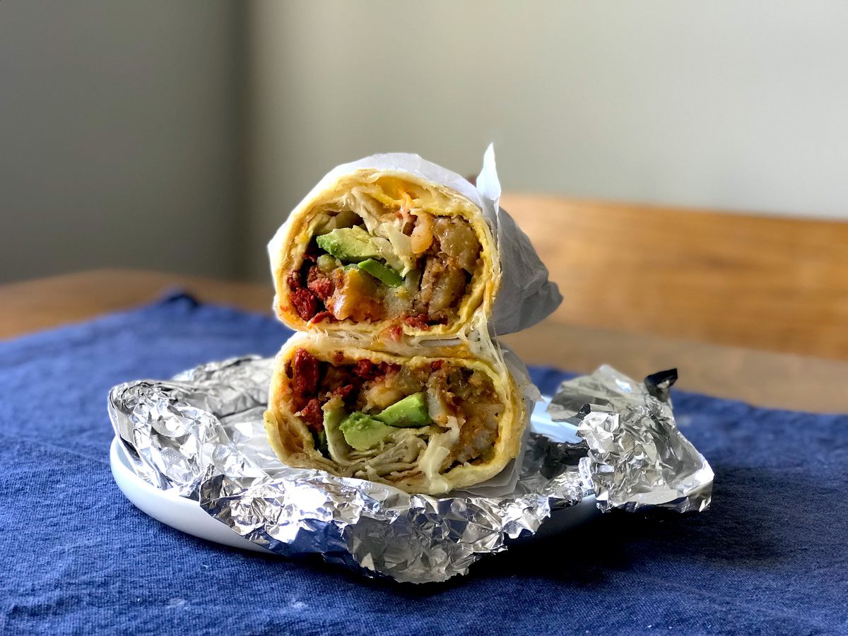 A breakfast burrito split in half and stacked on top of each other on top of tin foil on a plate.