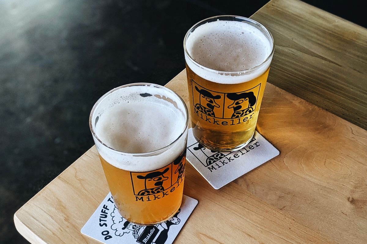 A picture of two pint glasses of Mikkeller beer on coasters, sitting on a wooden table at the Mikkeller pop-up space in Portland