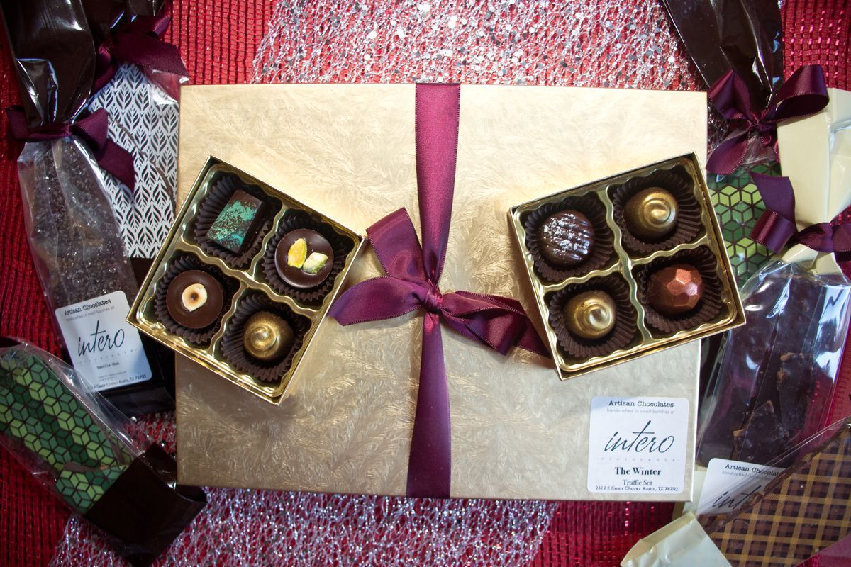 Two four-piece boxes of chocolate truffles on top of a golden box and flanked with bars of chocolate wrapped in plastic. 