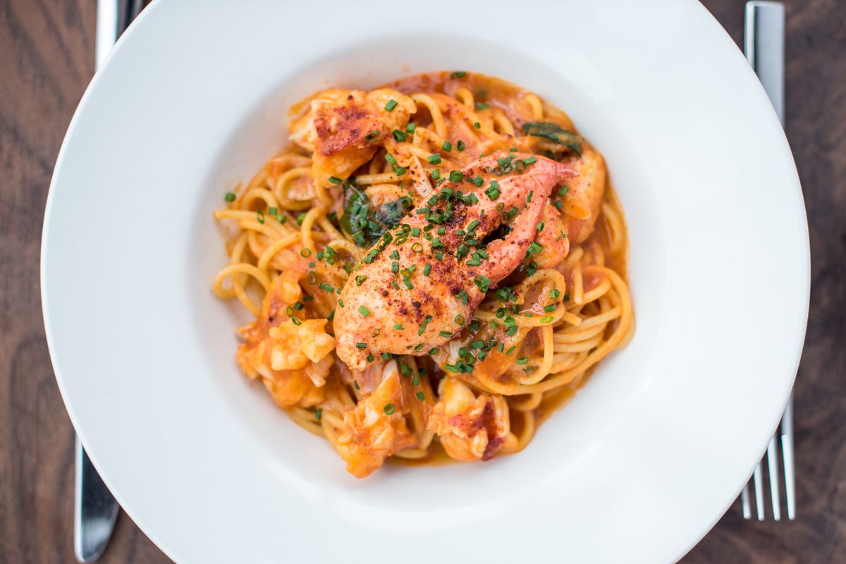 A white bowl filled with spaghetti with red sauce and lobster. 