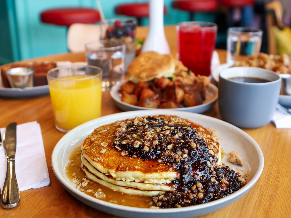 Fox Run’s lemon-ricotta pancakes with mixed-berry jam, brown sugar–oat streusel, and maple butter on a wooden table with orange juice, coffee, and an assortment of other breakfast dishes.
