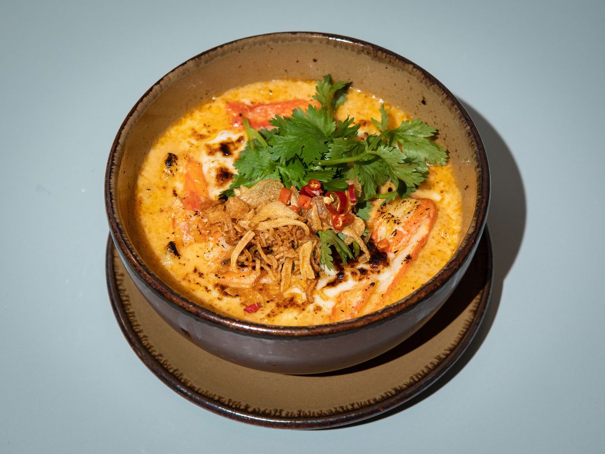 A bowl filled with yellow sauce, noodles, and crab, with green herbs sprinkled on top.