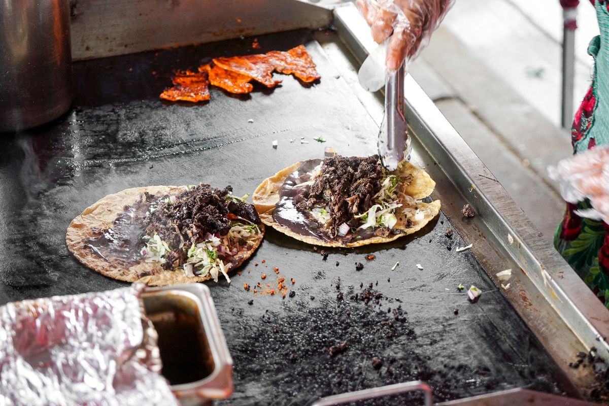 A cook prepares tacos on a steel griddle.