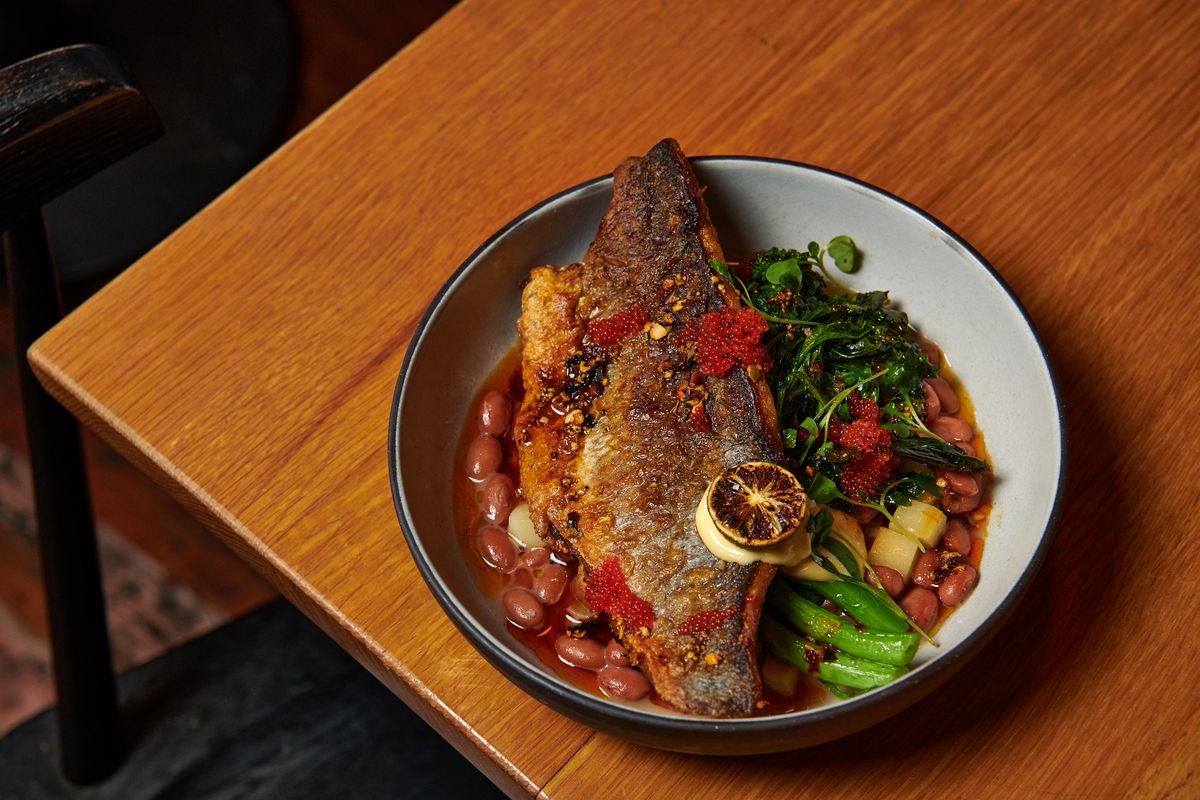 A crispy-skinned piece of white fish sits in a bowl with beans and rapini at Chelo.