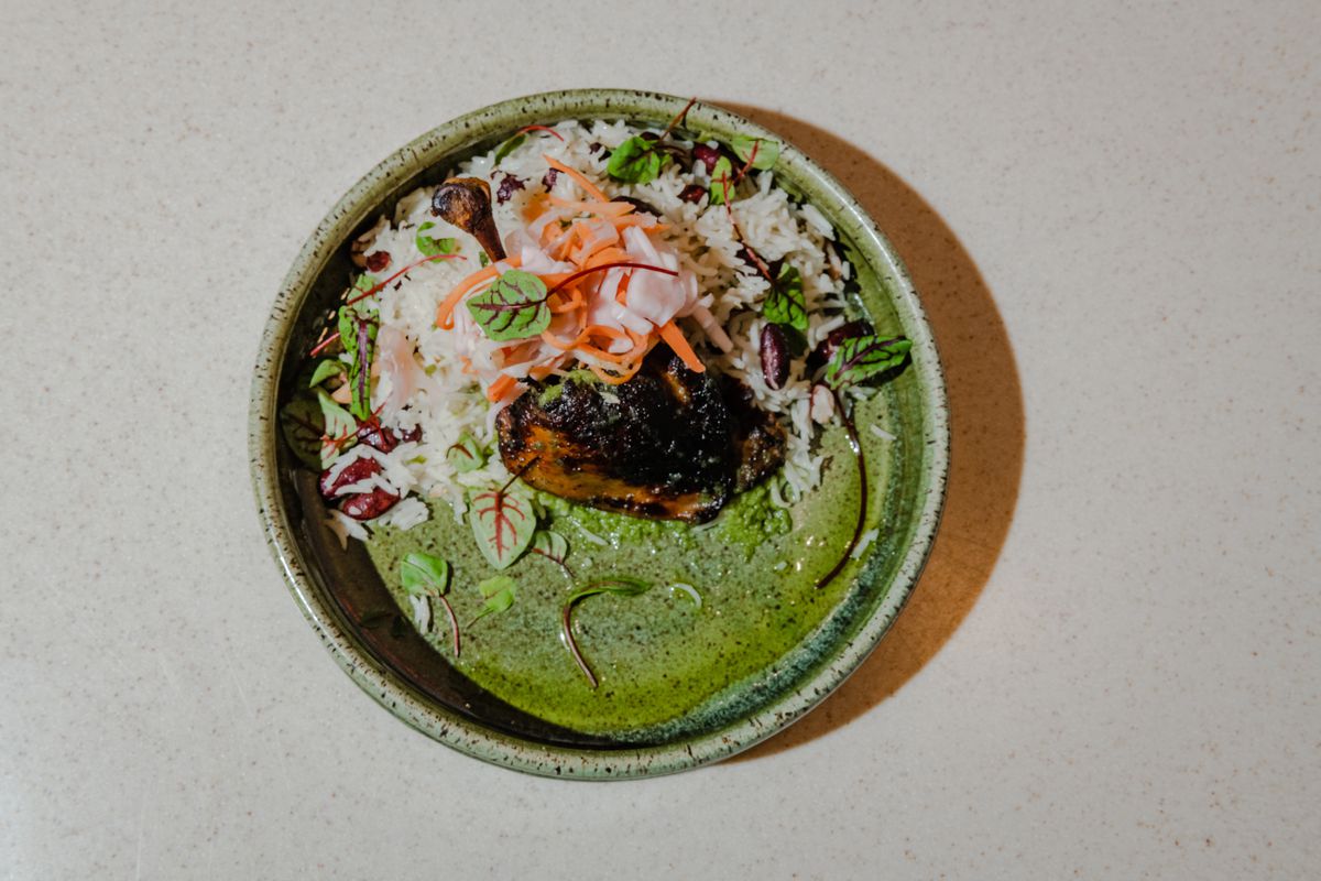 A green bowl filled with white rice, green herbs, and roasted duck.