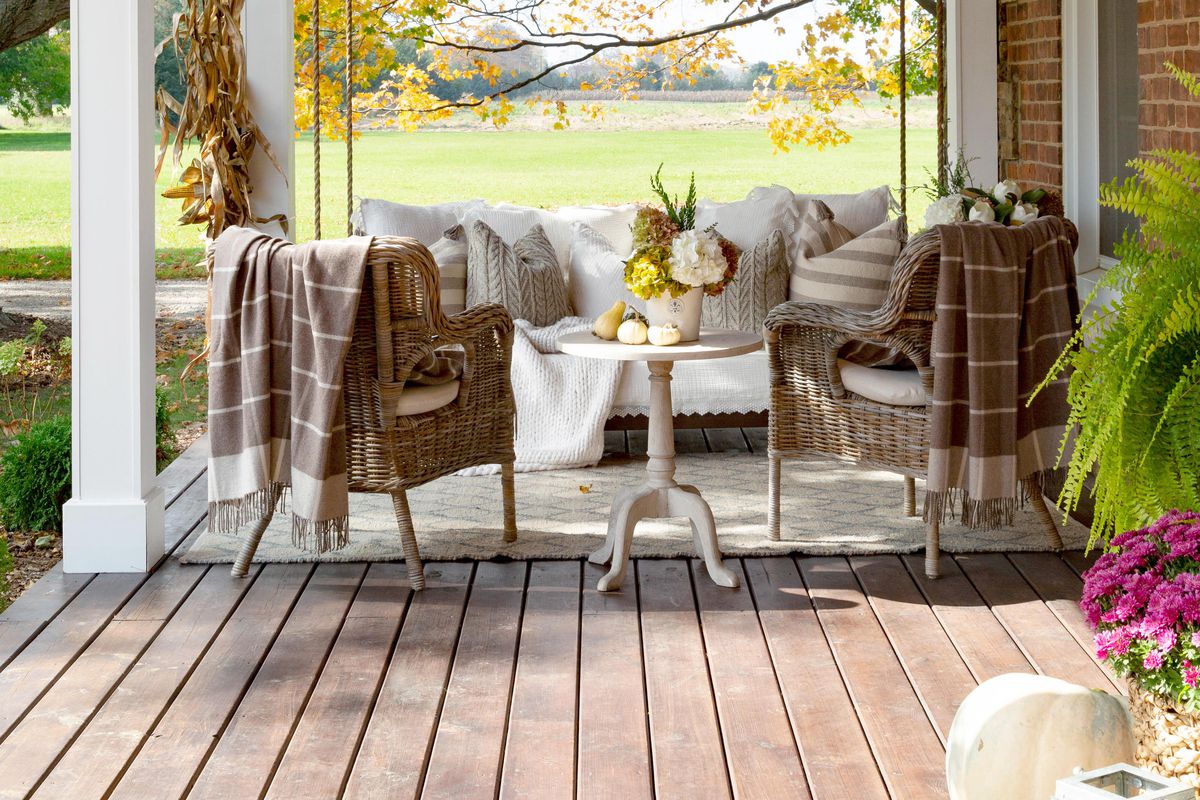 A front porch with a large swing, two wicker chairs and lots of cozy, warming decor. 