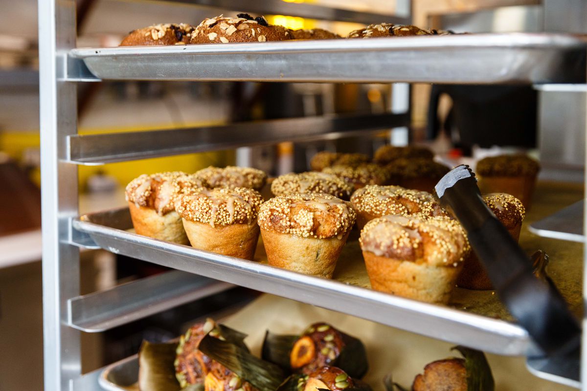 Three trays of muffins rest on a multi-tiered baking tray in a restaurant