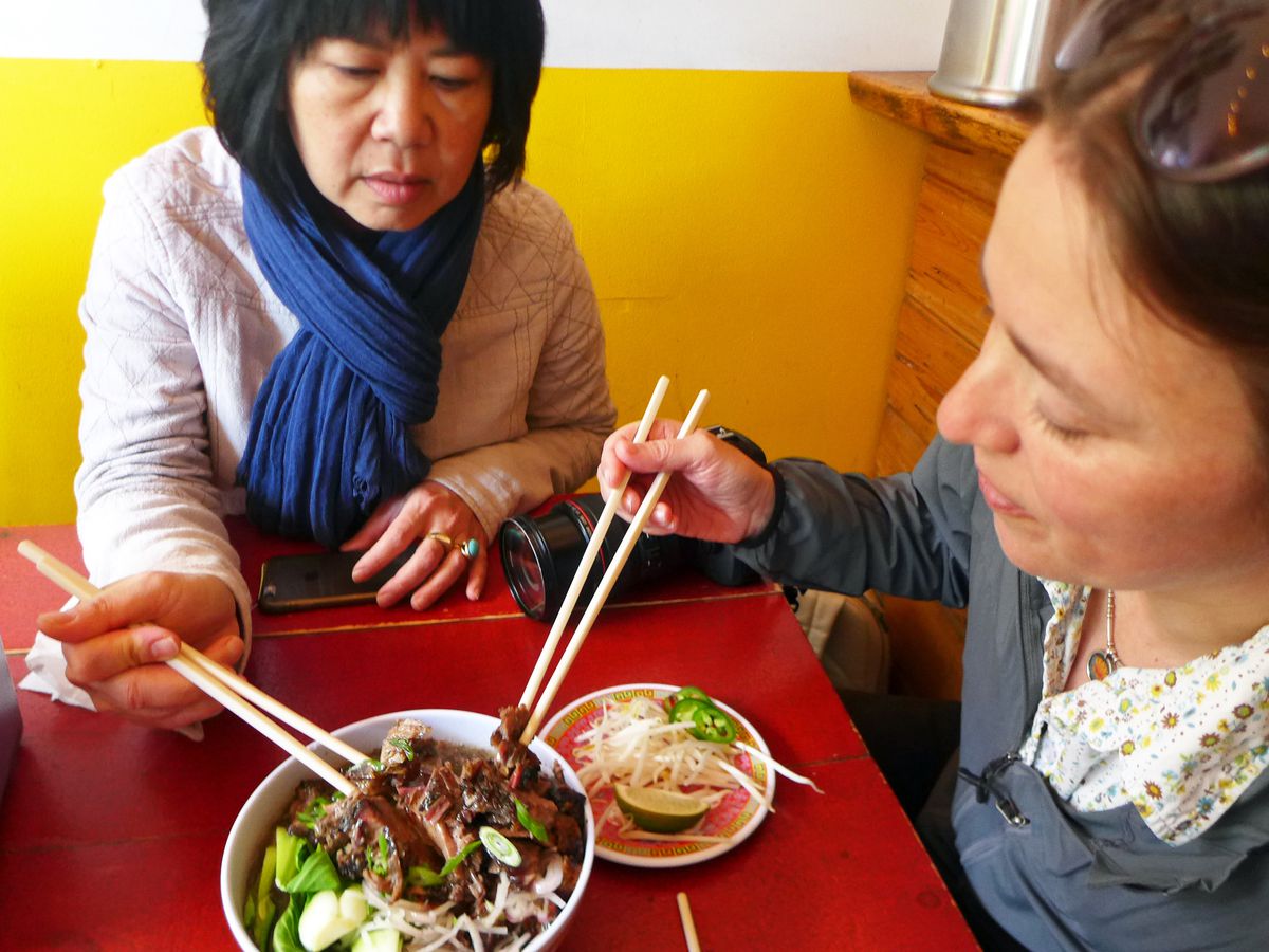Two diners with chopstick sharing a bowl of soup.