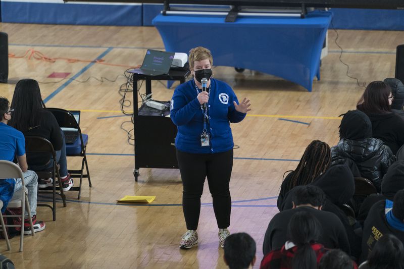 A school principal addresses her students during an assembly in a high school gymnasium.