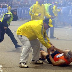In this Monday, April 15, 2013 photo, a race official assists Bill Iffrig, 78, of Lake Stevens, Wash., as Iffrig lies on the ground after the first explosion, as police officers react to a second explosion at the finish line of the Boston Marathon in Boston, Monday, April 15, 2013.  Iffrig, of Lake Stevens, Wash., was running his third Boston Marathon and near the finish line when he was knocked down by one of two bomb blasts. 