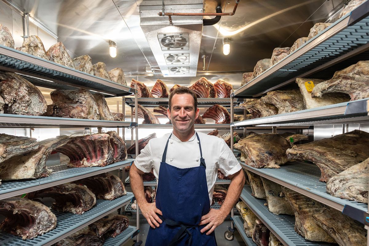 APL chef Adam Perry Lang stands inside his meat locker, hands on hips.