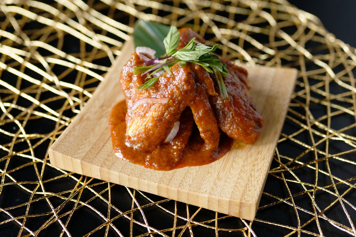 A small pile of chicken wings bathed in a brown sauce on top of a small, square wooden plate.