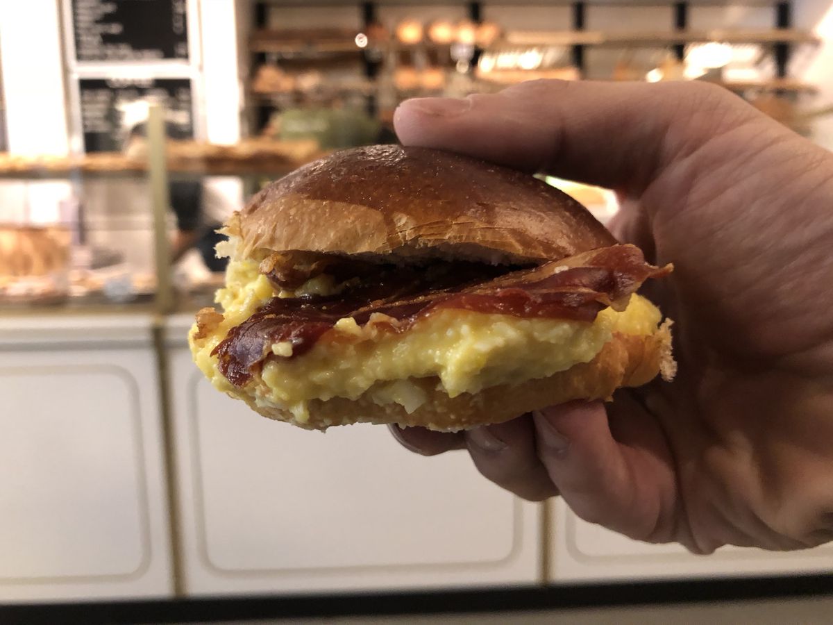 A small pancetta and egg sandwich is held in a hand.
