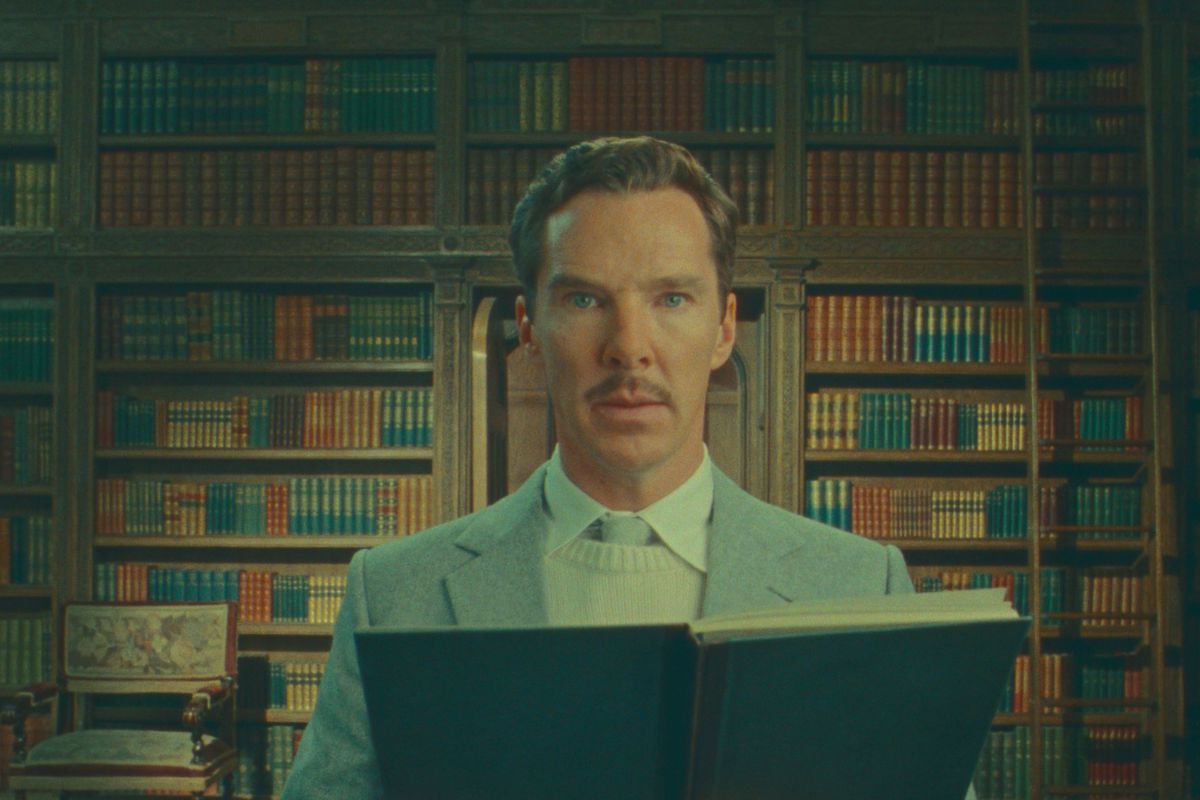 A man looks at the camera, with a wall of books behind him.