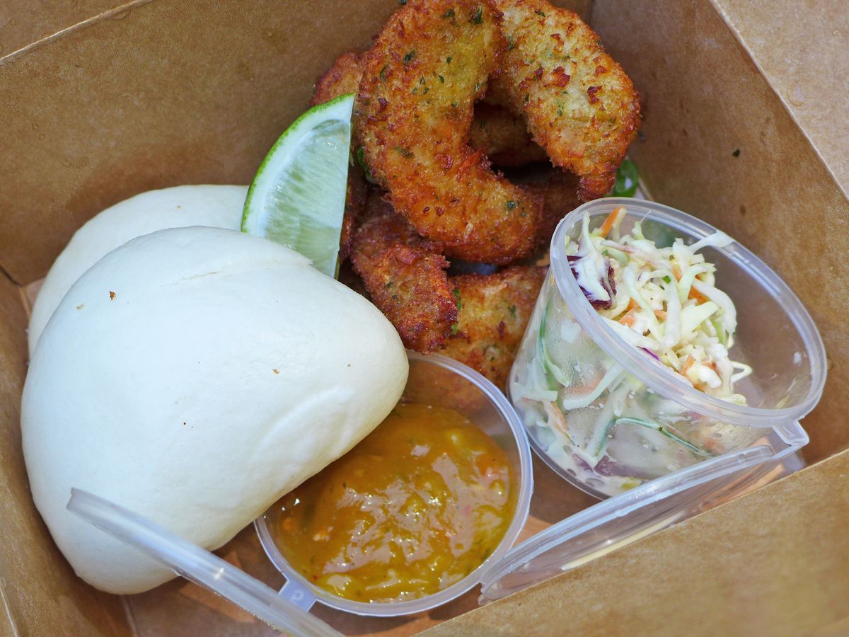 A brown box with steamed buns, slaw, sauce, and pile of fried shrimp.