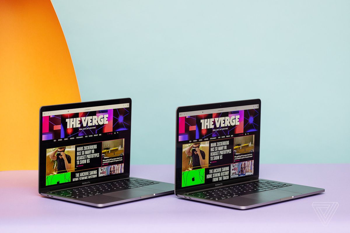Gli Apple MacBook Pro 2020 e 2022 aperti uno accanto all'altro e inclinati verso destra. Entrambi gli schermi visualizzano la homepage di The Verge.