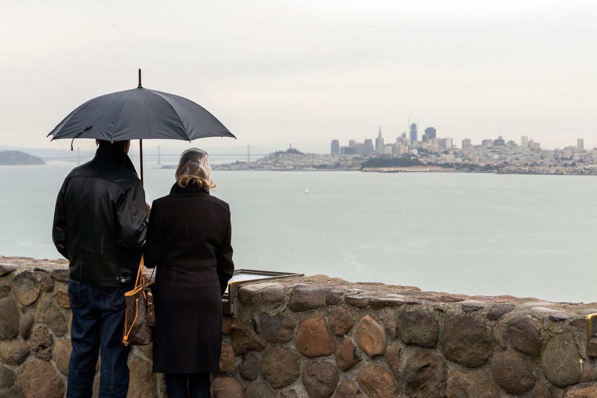 Tourists with umbrellas take a glimpse of San Francisco in the rain from the viewpoint at the Lone Sailors Memorial.