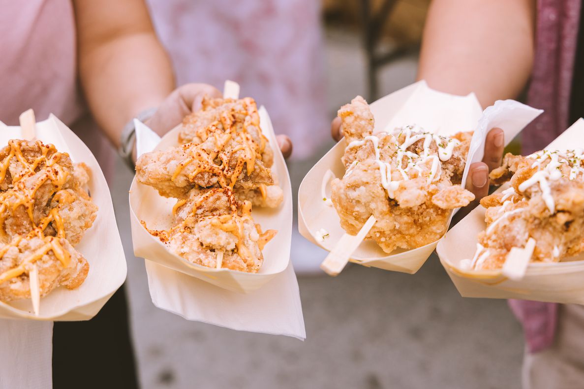 people holding four takeout containers containing fried food on skewers.