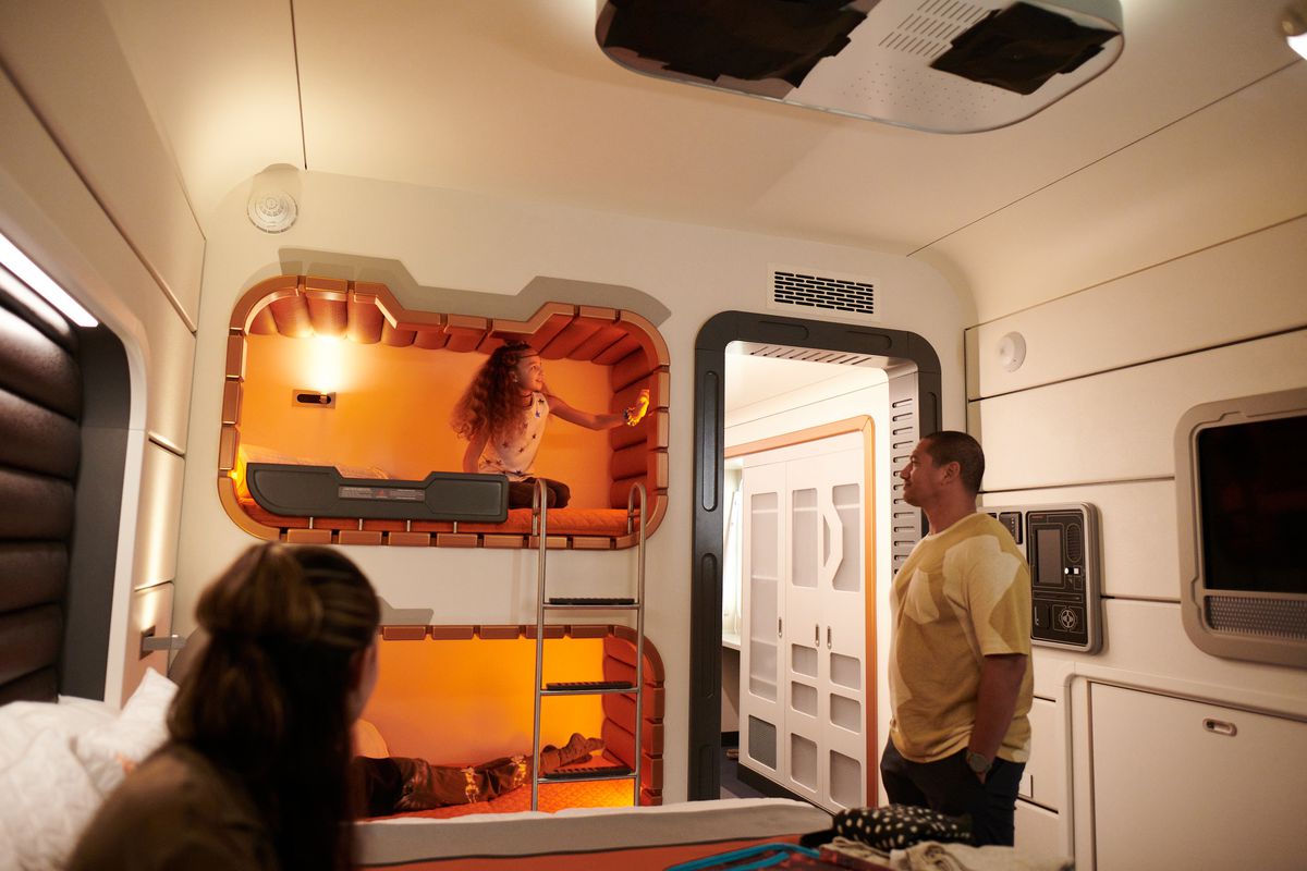 A little girl plays in an orange futuristic bunk bed with her parents watching on. 