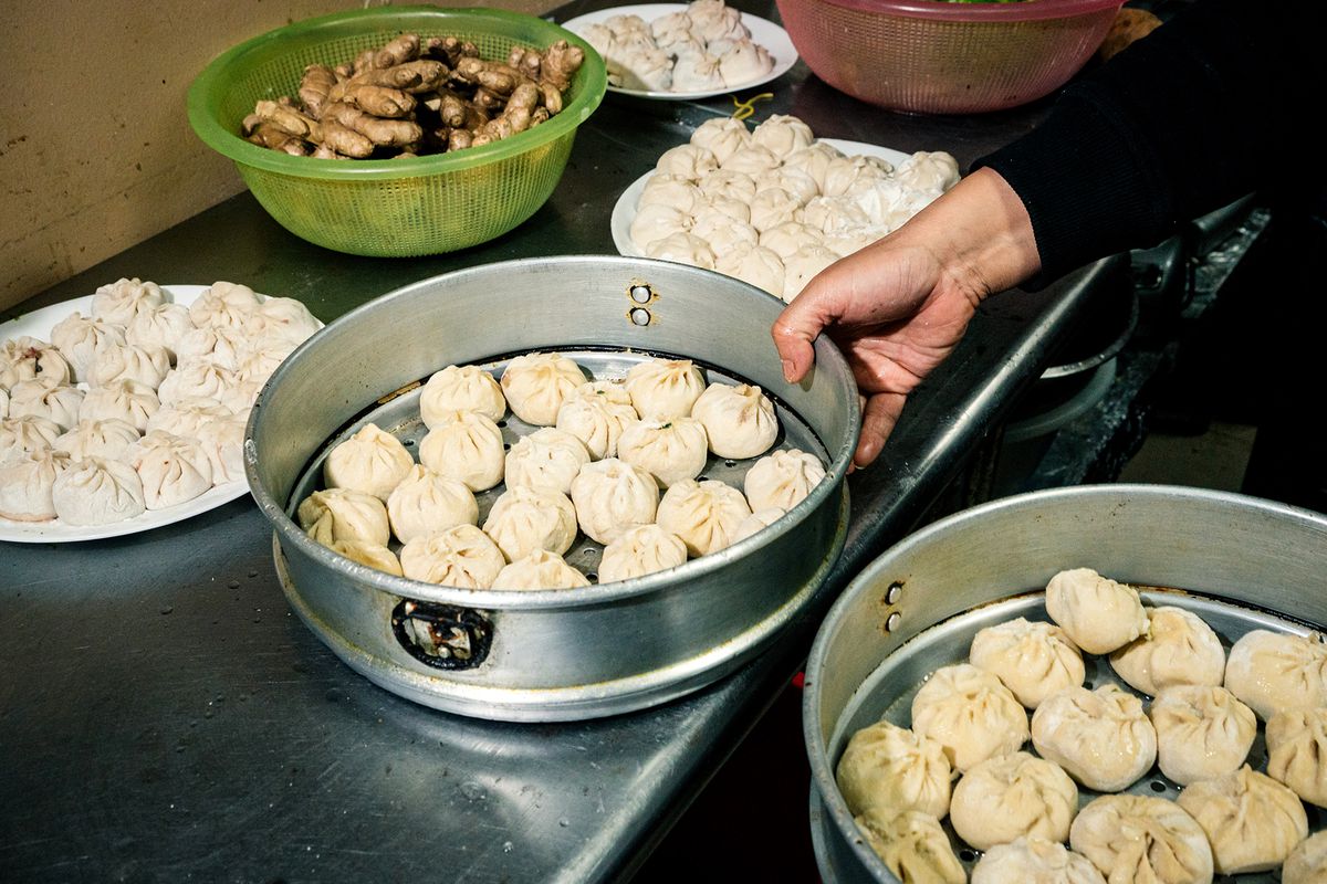 Large metal steam baskets of hand-folded dumplings are arranged in the kitchen.