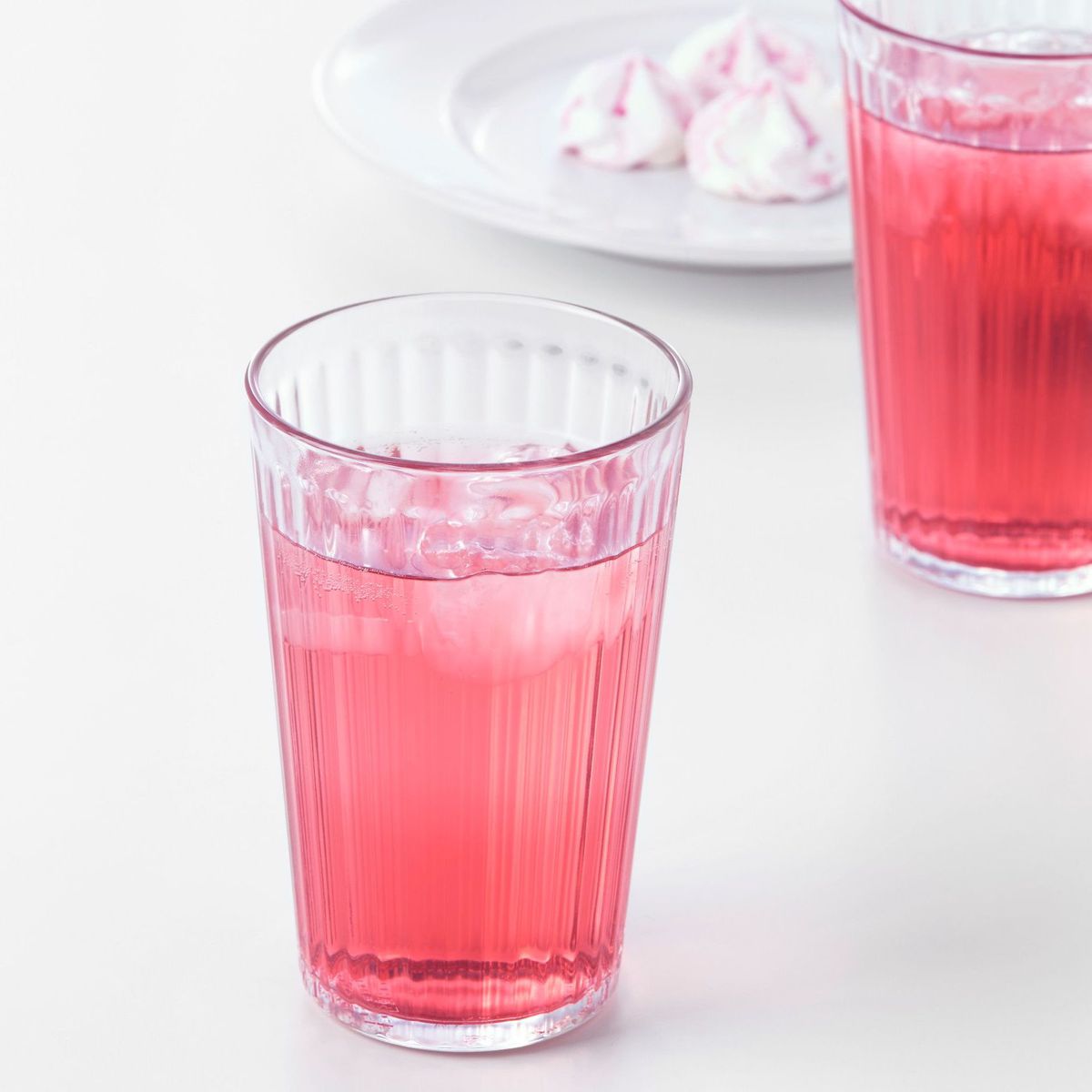 A tall glass has pink juice and ice inside. 