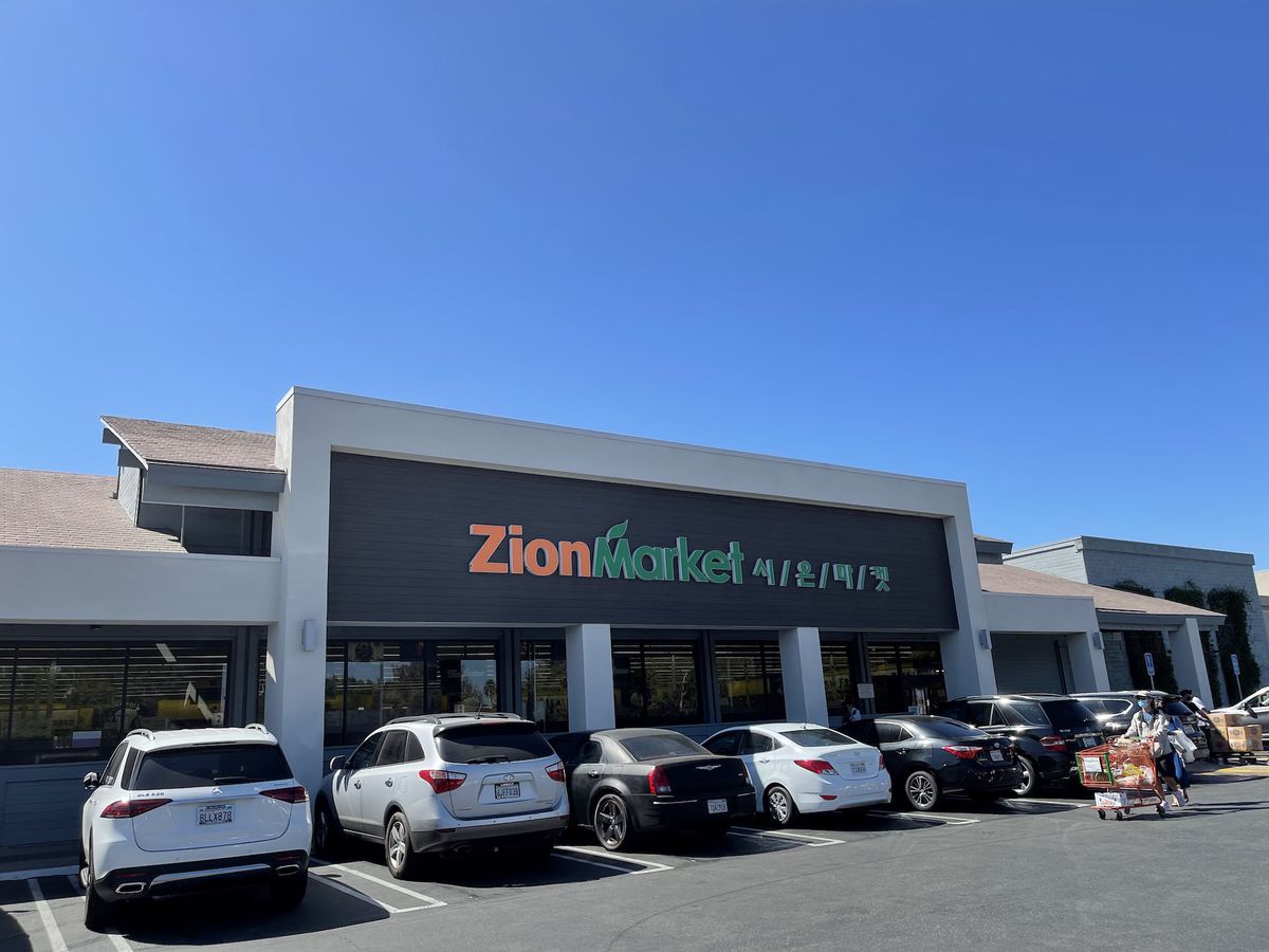 A clear blue sky backs the frontage for a store named Zion Market, as shown from the parking lot.